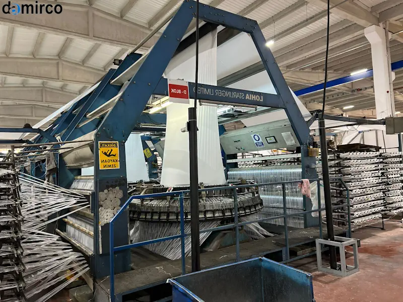 نمایی نزدیک از دستگاه اکسترودر در حال تولید توری پلاستیکی با نمایان شدن نقاط حرارتی و سیستم‌های کشش، نمادی از فرآیند پر انرژی تولید.