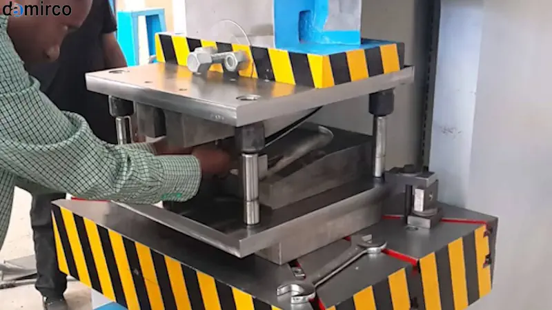 تصویر: نمای نزدیک از دستگاه پرس هیدرولیک در حال شکل‌دهی فلز، با نورپردازی متمرکز بر بخش‌های مکانیکی. در پس‌زمینه، نمودارهایی محو شده از مصرف انرژی و بهره‌وری نمایش داده می‌شوند که نشان‌دهنده بهینه‌سازی است.