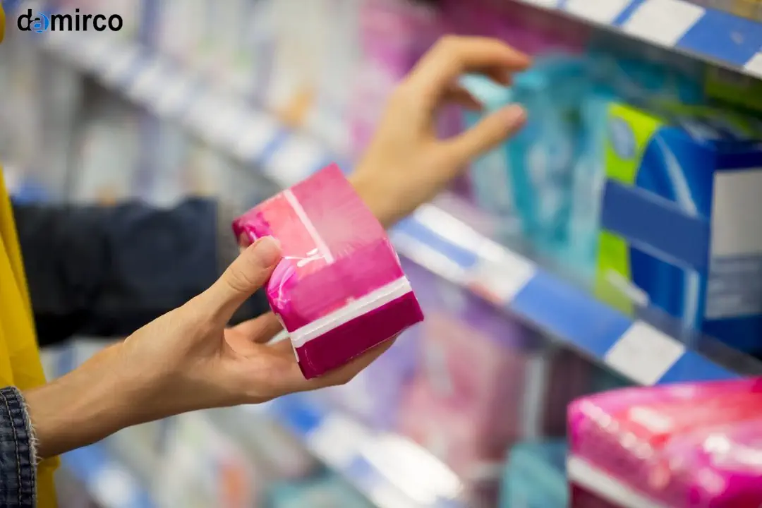 خط تولید نوار بهداشتی پیشرفته با ماشین‌آلات مدرن و اتوماتیک در یک کارخانه تمیز و نورانی، همراه با بسته‌بندی‌های نوار بهداشتی آماده در پس‌زمینه.