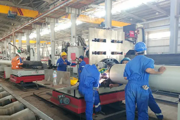 عکس چهار کارگر با لباس کار آبی در خط تولید اتصالات لوله