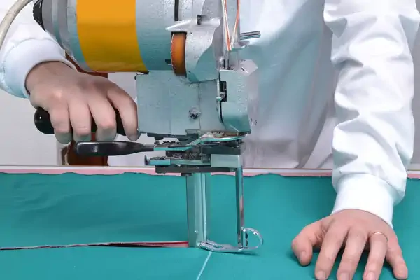 یک مردم در حال برش پارچه سبز با دستگاه برش پارچه لباس